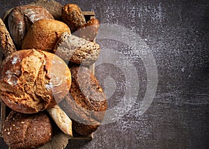 Background with Different Types of Bread put in a wooden box on dark surface, close up. Bakery concept. Empty space for text