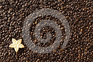 Background filled with a lot roasted coffee beans and a cookie