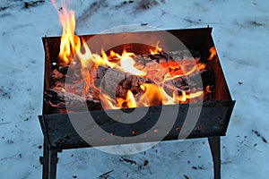 Background of fire and black wood. Dark grey, black white coals on bright fire inside metal brazier. Wood burning in the brazier.