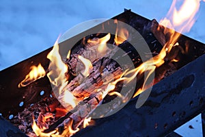 Background of fire and black wood. Dark grey, black white coals on bright fire inside metal brazier. Wood burning in the brazier.