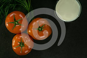 Background food ingredients on black table. Fresh tomatoes and greens, a glass of milk.