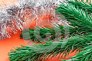 Background in the form of Christmas tree decorations - a green branch of artificial spruce and silver rain on a coral background,
