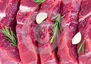 Background of fresh raw sliced beef steaks, garlic, rosemary and