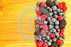 Background with fresh summer berries on a bamboo chopping board. Raspberries, blueberries, and blackberries groupped on the right