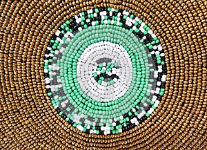 Background of geometric pattern of gold, green, white, and black beadwork with rows of circular patterns