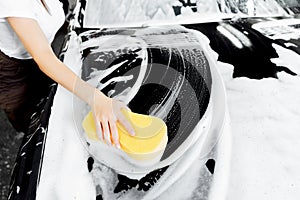 Background hand hold sponge over black car for washing white foam
