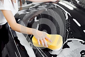 Background hand hold sponge over black car for washing white foam. Top view