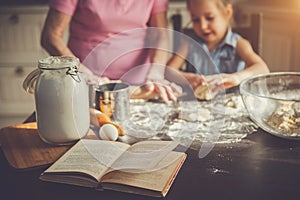 Background image cookbook, table, rolling pin, focus on the foreground. Girl and her grandmother cooking on kitchen.