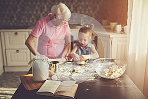 Background image cookbook, table, rolling pin, focus on the foreground. Girl and her grandmother cooking on kitchen.