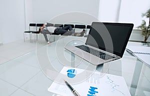 Background image of a laptop on a glass table in an empty office