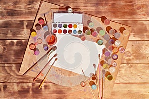 Background image showing interest in watercolor painting and art. A blank sheet of paper, surrounded by brushes, cans with waterc
