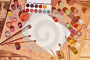 Background image showing interest in watercolor painting and art. A blank sheet of paper, surrounded by brushes, cans with waterc