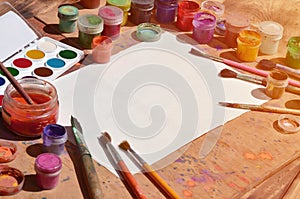 Background image showing interest in watercolor painting and art. A blank sheet of paper, surrounded by brushes, cans with waterc