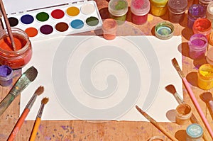 Background image showing interest in watercolor painting and art. A blank sheet of paper, surrounded by brushes, cans with waterc