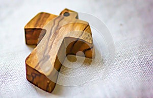 Background, image of a small wooden cross laid on linen fabric used as a pendant by some faithful.