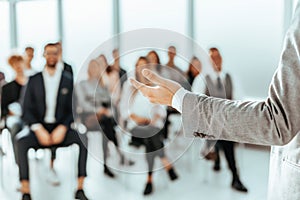 Background image of a speaker standing in front of listeners in a conference room