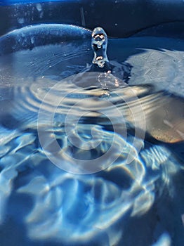 Background image of water droplets falling on water in a blue container and splashing up.