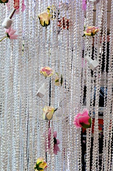 Background with a large white woven curtain made of twisted ropes, decorated with flowers and bottles of nail polish. The curtain