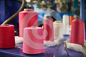 Background with a lot of pink and white coils with threads. Bobbins are stacked in a rows, one on the other. Selective focus