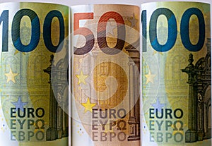 The background is made of paper money in denominations of 100 and 50 euros, each rolled into a roll. Close-up