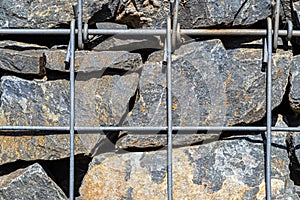 Background made of a stone wall secured with a galvanized metal mesh, close-up shot.