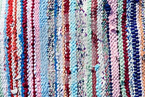 Background of manually woven textile materials of different colours, red, green, yellow, blue, green and pink pieces, with vertica