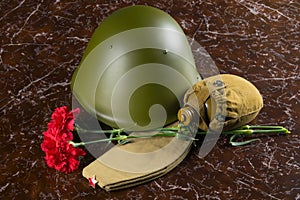 On the background of the monument, two red carnations, water flask, military helmet and cap