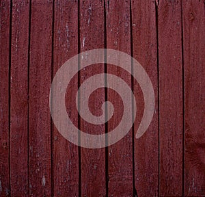Background of old fence boards with red paint cracked from time to time. Close-up on weather-peeled boards with red