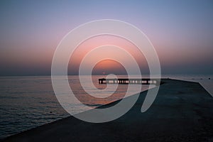 Background with old wooden pier in the sea at sunset. The sun goes down in the water