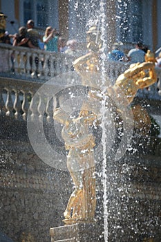 Background photo: a vertical fountain stream against the background of golden sculptures of the Grand Cascade fountain