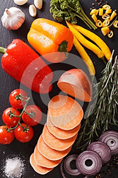 Background of raw vegetables: sweet potatoes, peppers, tomatoes, onions, garlic, rosemary and spices. vertical top view