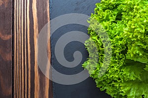 Background with salad. A bunch of green lettuce on a black slate stand on a wooden tabletop