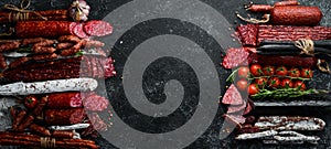 Background of salami, sausages and meat products, on black stone background. Top view.