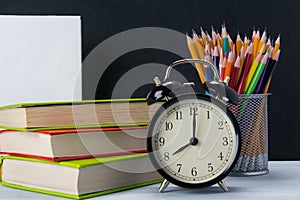 Background of sets of office items and a black alarm clock on colorful books, next to a glass with pencils, there is a place for