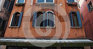 Background shot, camera slowly slides by beautiful old historic red building with windows open on Venice canal, Italy.