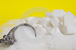Background of sugar cubes and sugar in spoon. White sugar on yellow background.