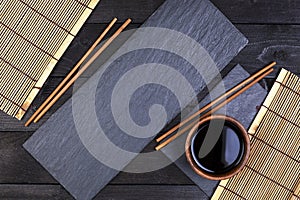 Background for sushi. Bamboo mat, soy sauce, chopsticks on dark table.