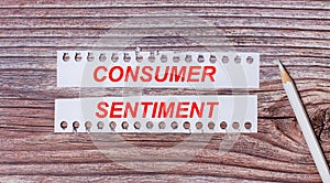 Background for text. White strips of paper with the text CONSUMER SENTIMENT and a white pencil next to it on a wooden background