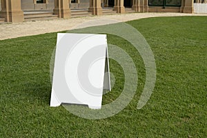 Background texture of a blank white advertising information board place outdoor on green and healthy grass lawn.