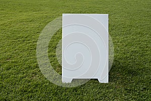 Background texture of a blank white advertising information board place outdoor on green and healthy grass lawn. Mockup template