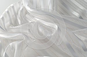 Background texture, pattern. White silk fabric, with a light strip. Closeup of rippled white silk fabric. Smooth elegant golden s