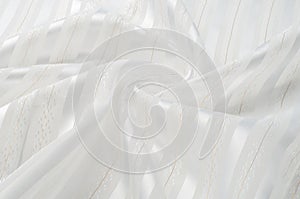 Background texture, pattern. White silk fabric, with a light strip. Closeup of rippled white silk fabric. Smooth elegant golden s