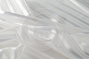 Background texture, pattern. White silk fabric, with a light strip. Closeup of rippled white silk fabric. Smooth elegant golden s