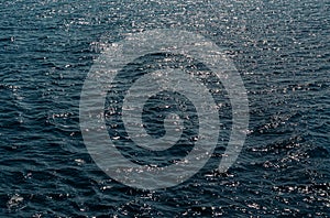 Background of transparent blue sea water top view. Water ripples and pattern on ocean surface with sunlight reflection