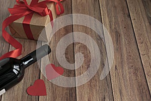 Background for Valentine`s Day. A bottle of wine, a gift from kraft paper, a heart and a satin red ribbon on a wooden background