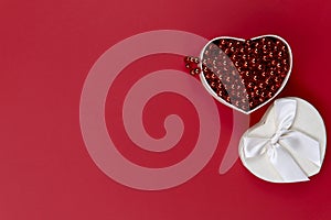 Background of Valentine`s Day. On a red background on the right is an open white gift box with red beads.