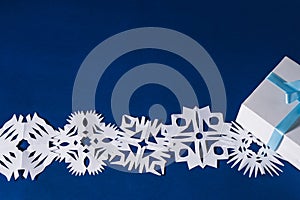 Background of various Christmas themed snowflakes cut out of white paper on a trendy blue background 2020 with a gift