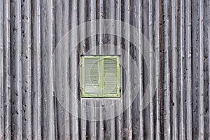 Background of a weathered wooden wall with vertical wooden slats and an old window with closed green shutters in it