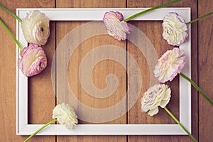 Background for wedding or party invitation. Picture frame with flowers on wooden table. View from above