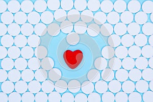 Background of white pills macro with a red heart lying on a blue background, top view.